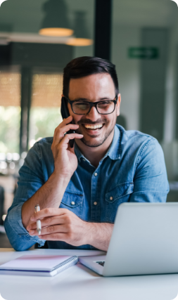 Portrait of young smiling cheerful entrepreneur in casual office making phone call while working with laptop